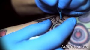 Фото процесса нанесения татуировки на кожу. Мастер в голубых перчатках работает тату-машинкой над эскизом, создавая яркий рисунок.
